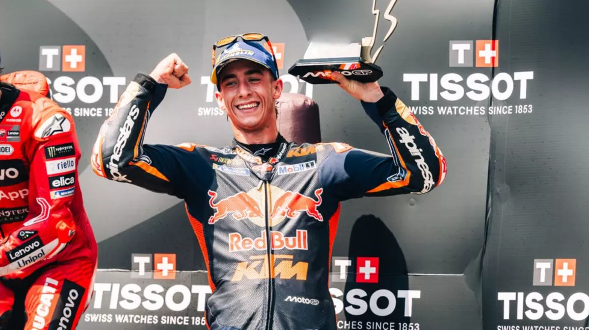 Pedro Acosta sul podio MotoGP 2025 con la tuta Red Bull KTM, trofeo in mano e braccia alzate in segno di vittoria.